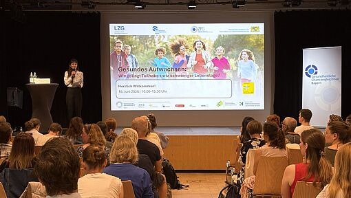 Vortragende steht vor Publikum in einem Saal mit einer Präsentation zum Thema Gesundes Aufwachsen auf der Leinwand