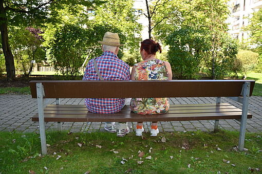 Ältere Frau und älterer Mann sitzen mit dem Rücken gerichtet zusammen auf Parkbank